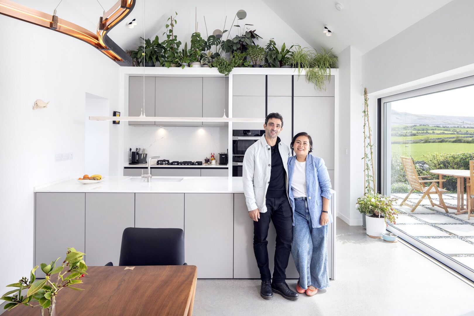 Richard and Boo in the kitchen designed by Arena Kitchens. Boo is a fantastic cook and sells her spice mixes and curries locally. She is also a wonderful gardener and plantswoman. She uses a ladder to reach the plants at ceiling height. The crab on the wall is a nod to her pet name Boo &ndash; which means crab. Her real name is Rapeepan. Photo: Tony Gavin